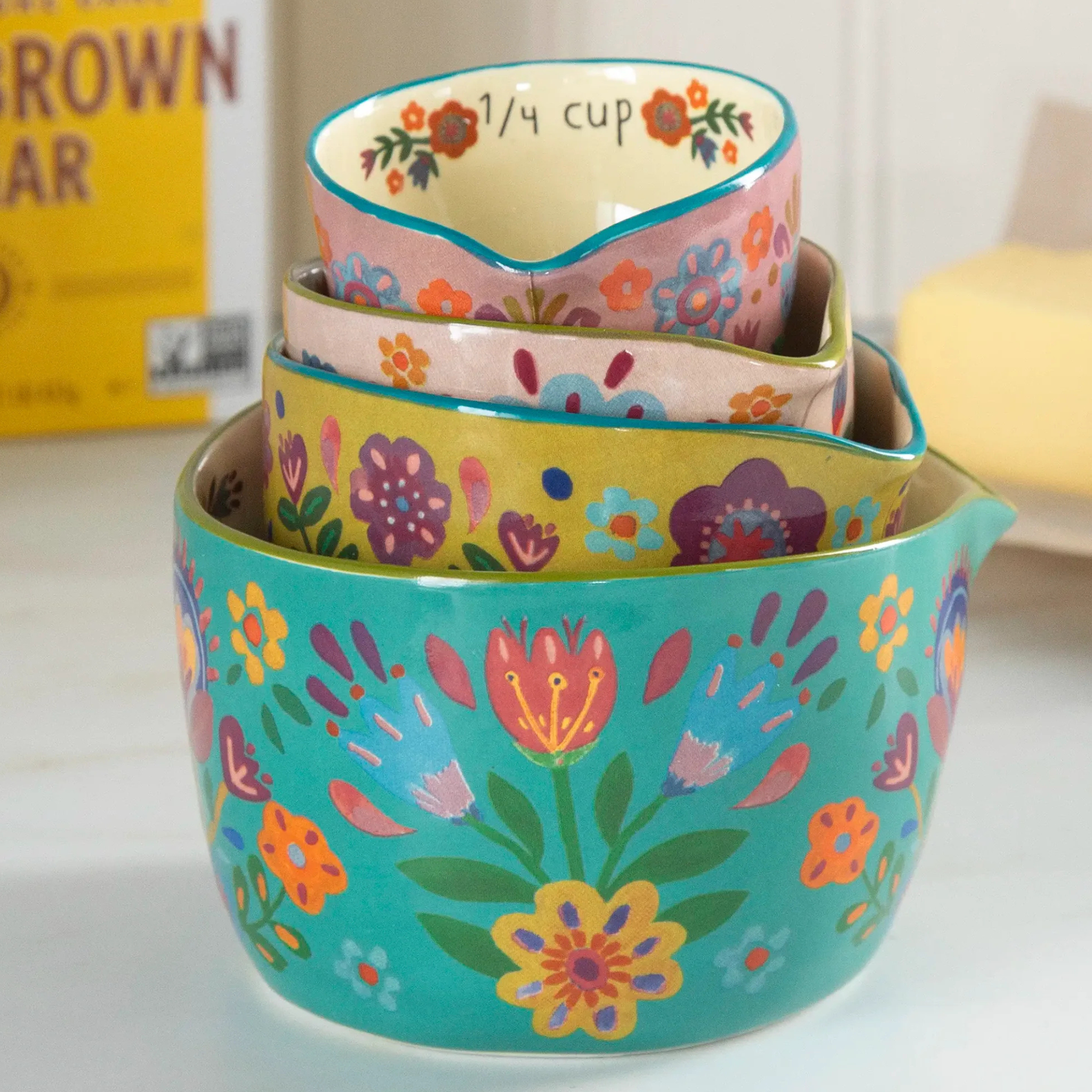 Ceramic nesting measuring cups in Folk Flower design by Natural Life, featuring colorful floral patterns and varying sizes.