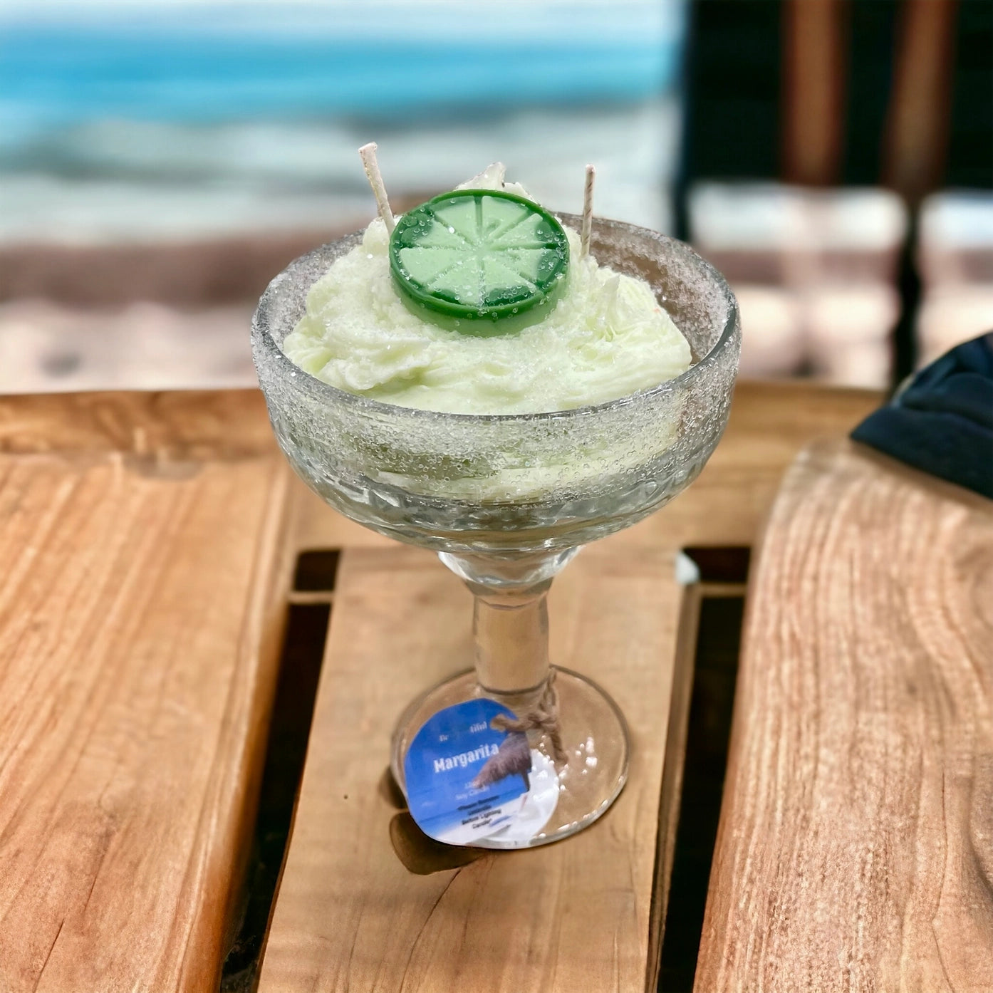 Green margarita candle with a lime wedge on a wooden table by the beach