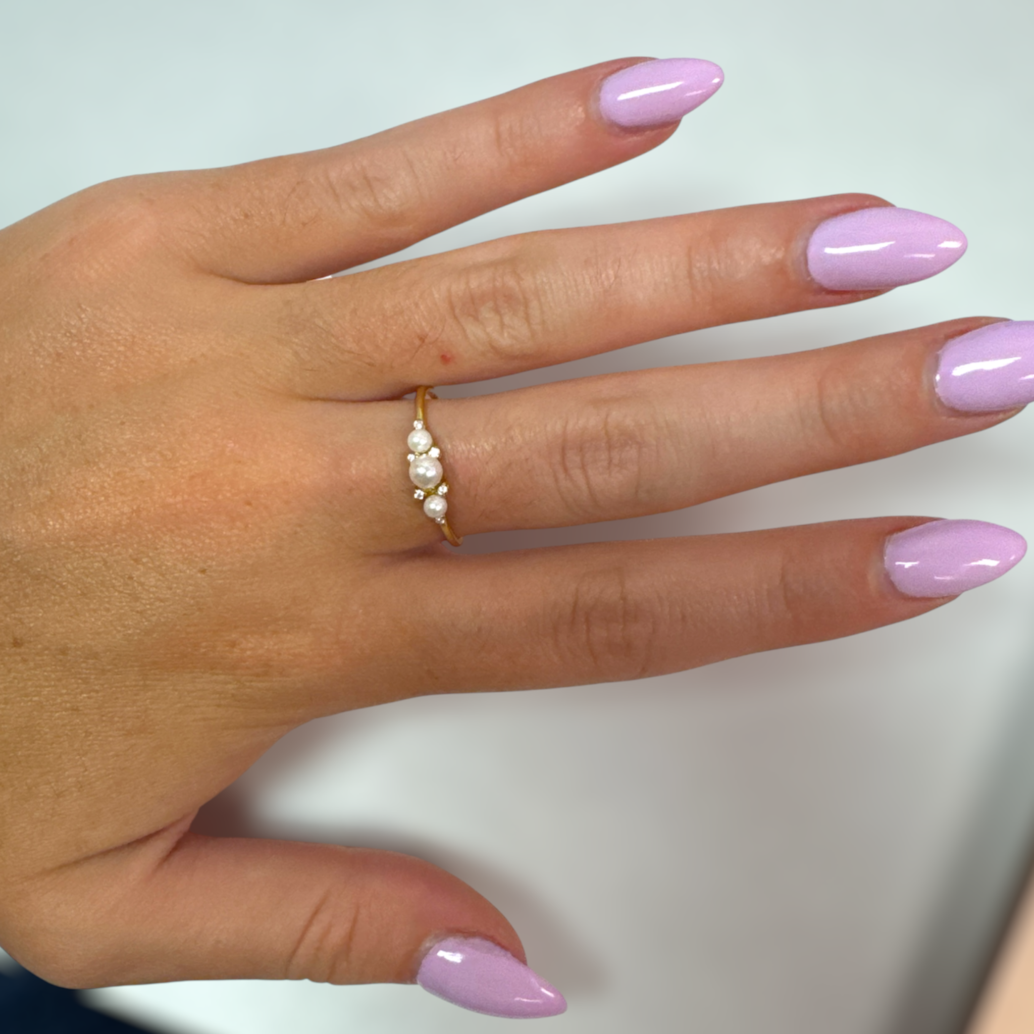Gold Princess Pearl ring worn on a hand with pink nail polish against a white background.