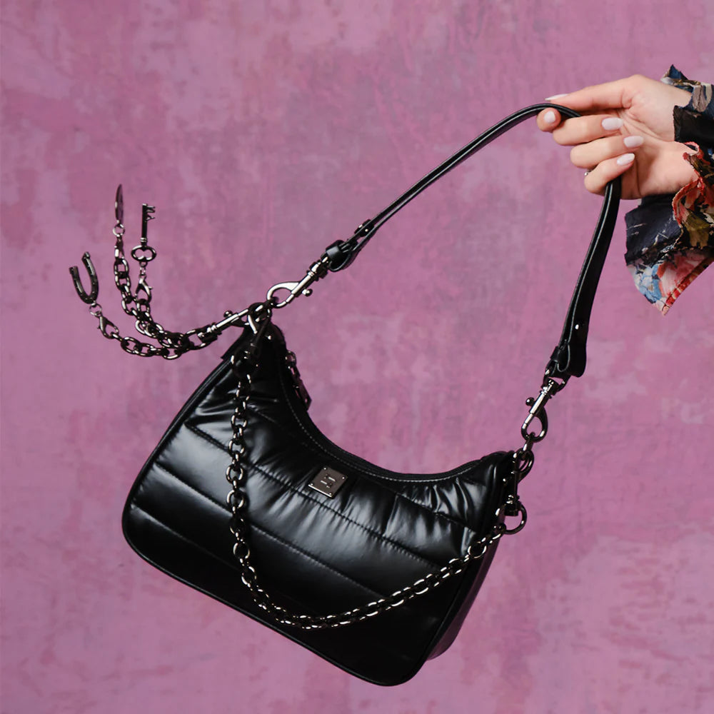Black quilted Think Royln shoulder bag with chain details, held by a hand against a pink background.