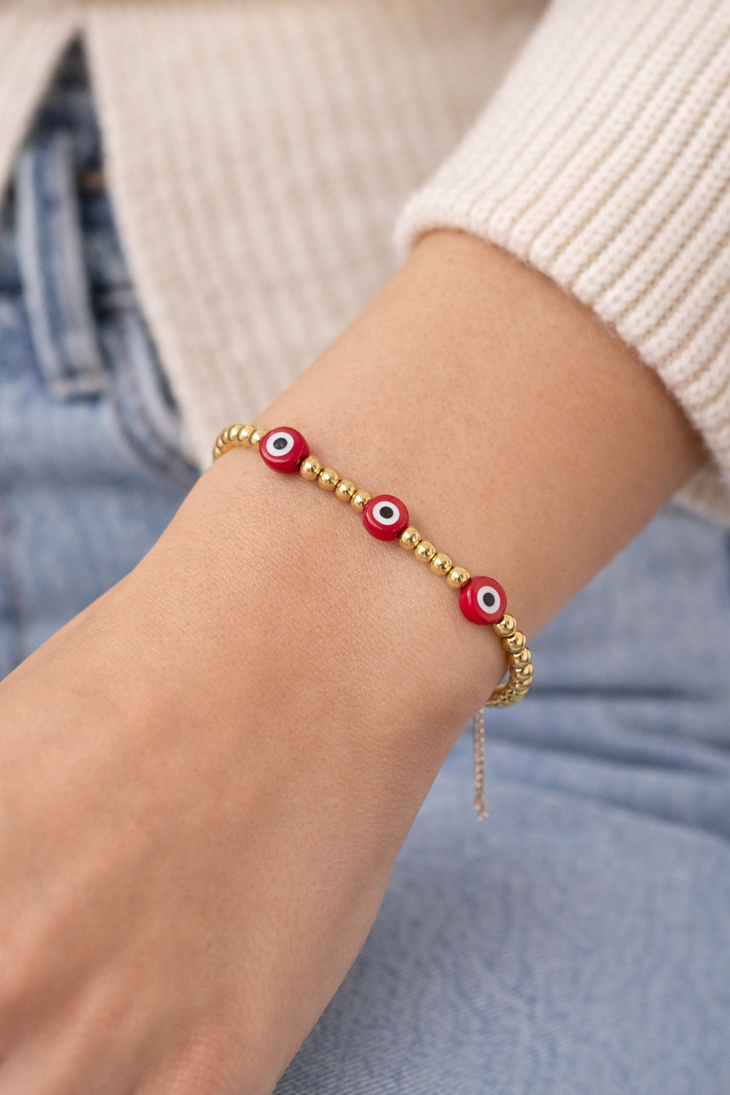 Evil eye bracelet by The Skylar Project featuring red and gold beads worn on a wrist.