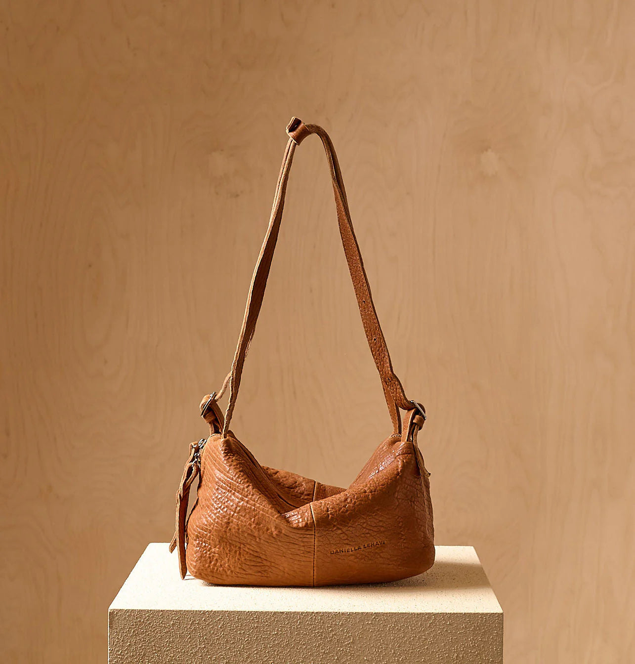 Brown leather handbag on a beige pedestal against a beige background