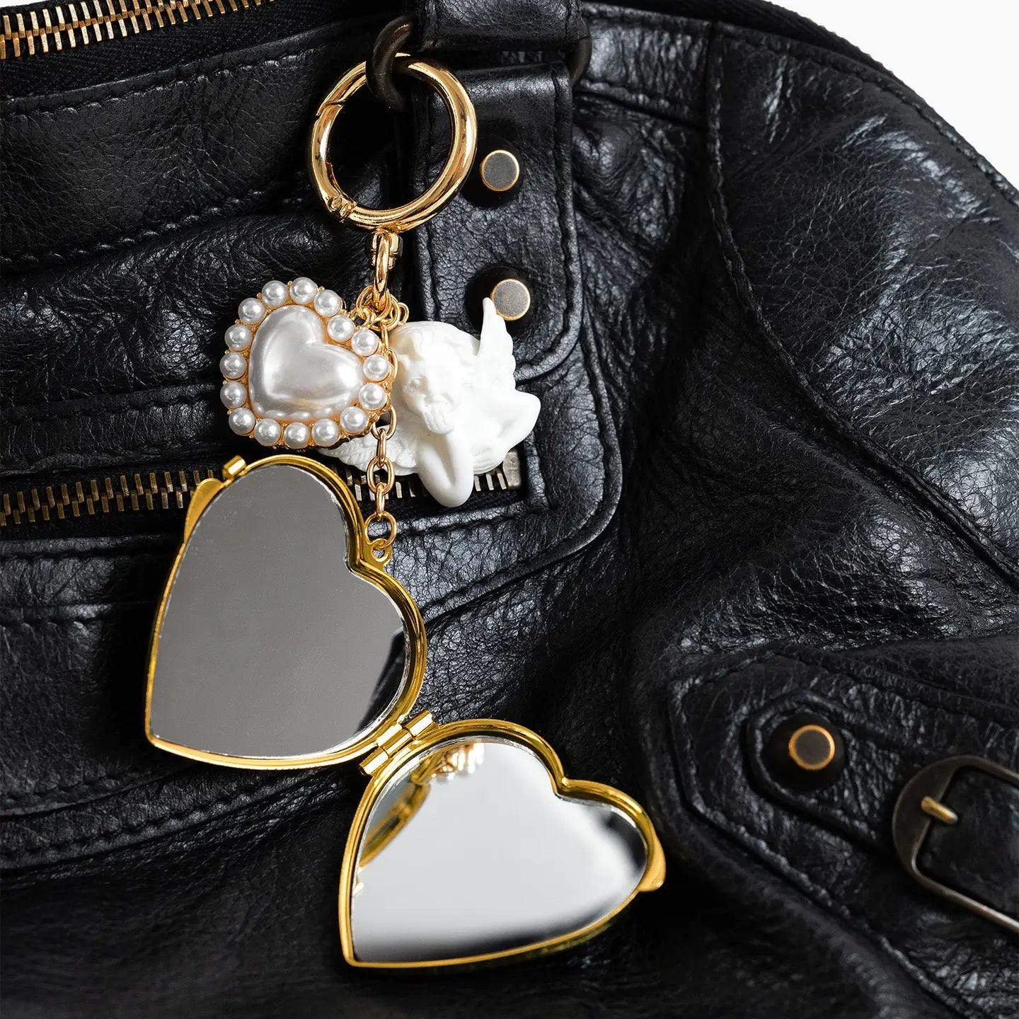 Heart-shaped Angel Kiss mirror locket bag charm with pearl on black leather background.