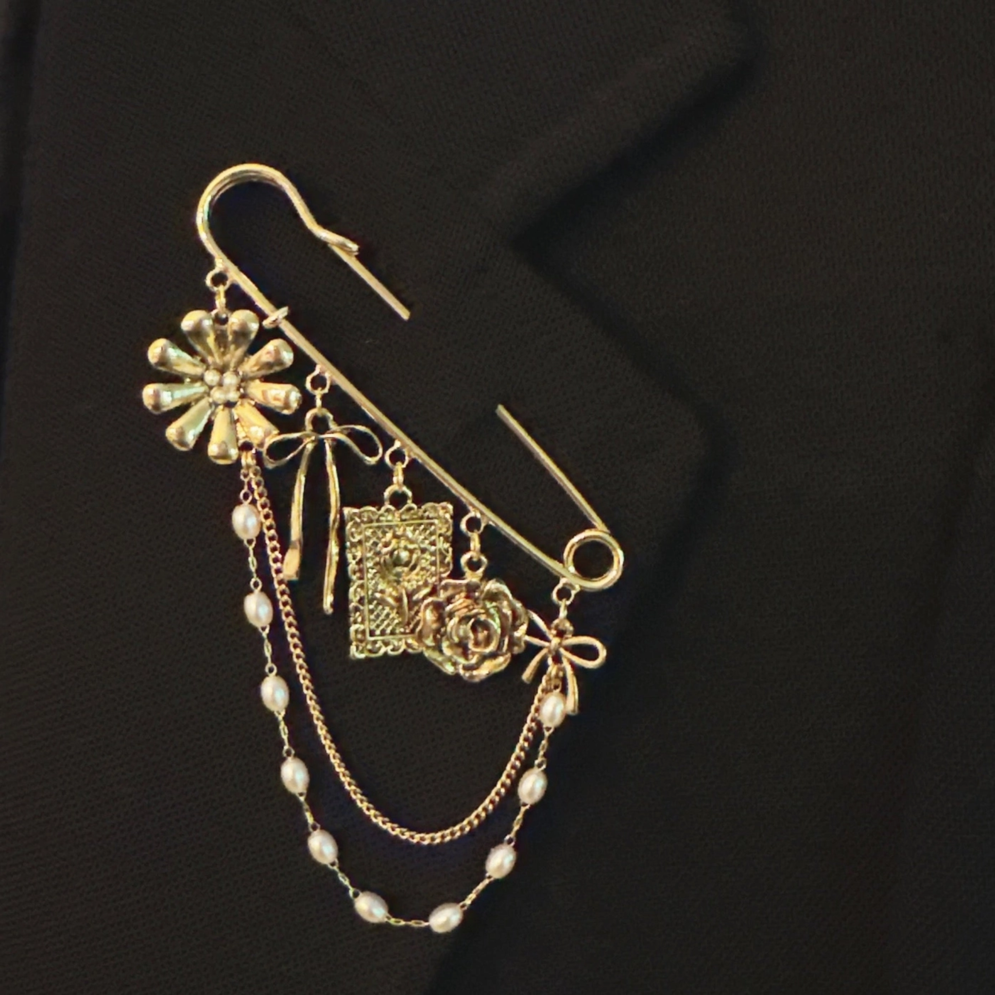 Elegant gold floral ribbon brooch by Ellison + Young with charms, pearl chains, and safety pin design for sophisticated accessory.