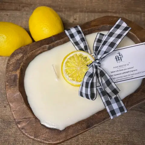 Candle with lemon slice and checkered ribbon on a wooden tray with lemons in the background