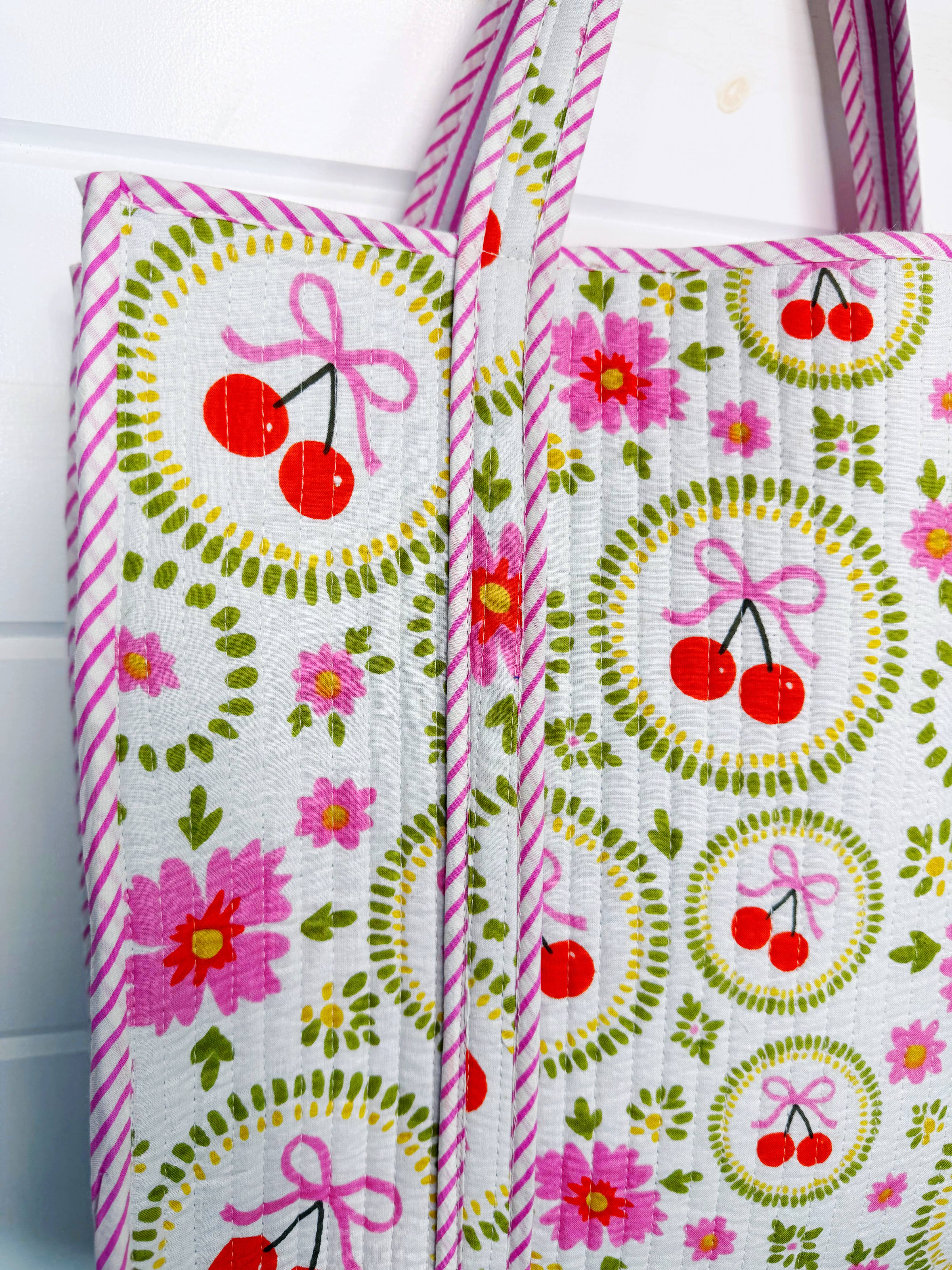 White quilted tote bag with cherry and bow design from Folklore Couture, large travel tote with spacious interior and stylish accents.