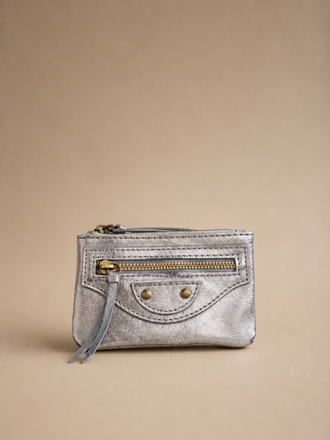 Silver metallic wallet with a gold zipper on a beige background